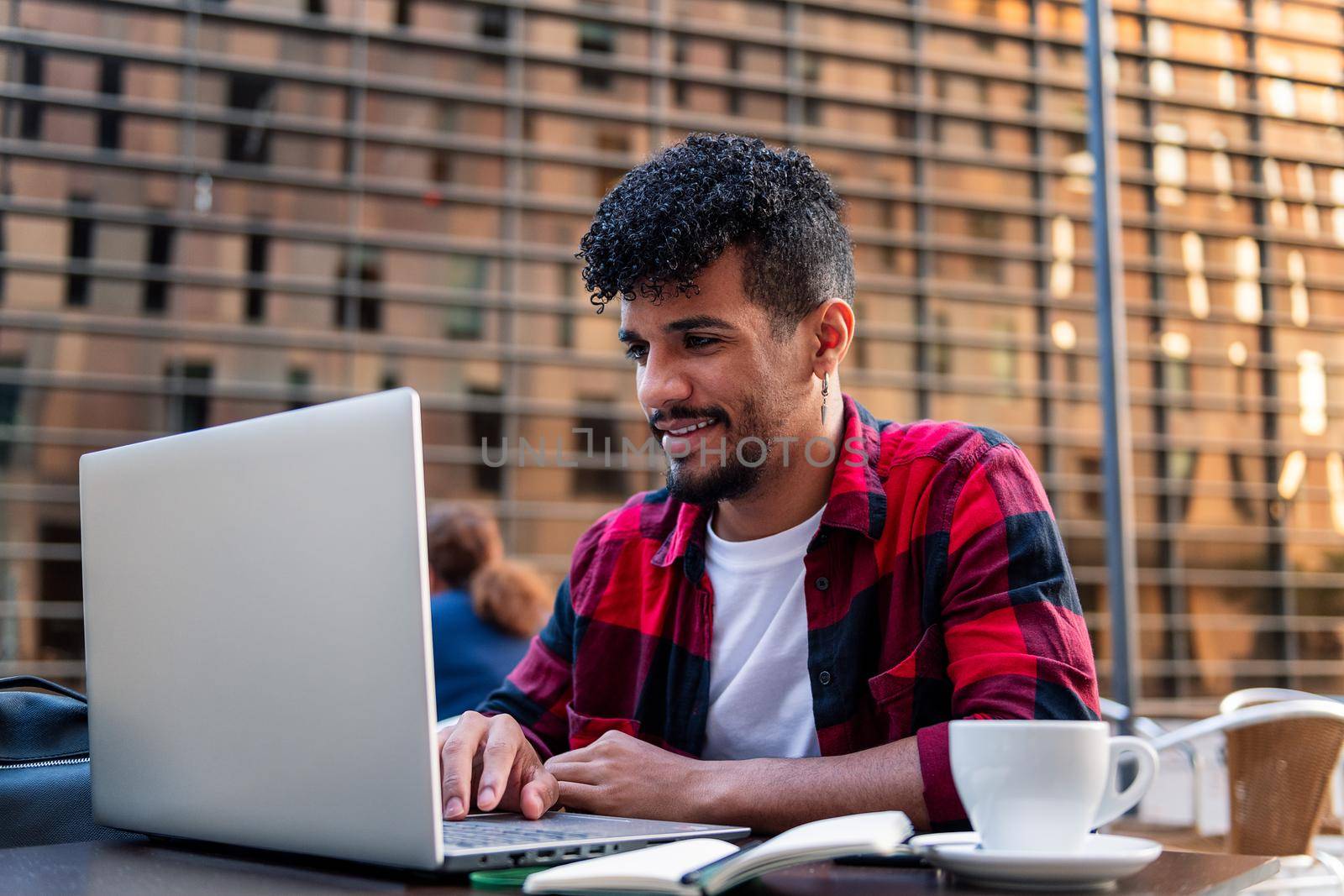 young latin man working with his computer on the terrace of a coffee shop, concept of technology and urban lifestyle