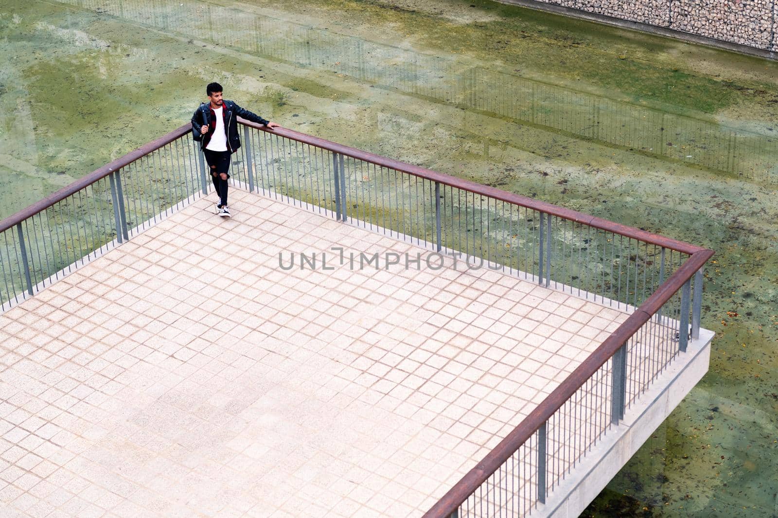 young urban man resting leaning on the railing next to the lake in a park of the city, concept of urban lifestyle