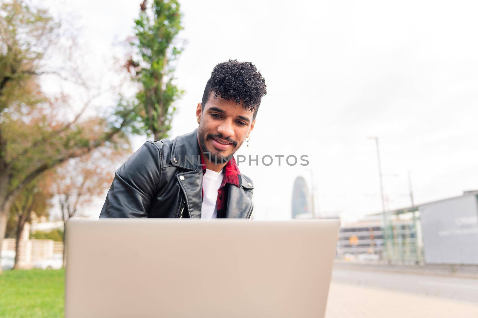 young latin man working on his laptop computer sitting on a city bench, concept of technology and urban lifestyle