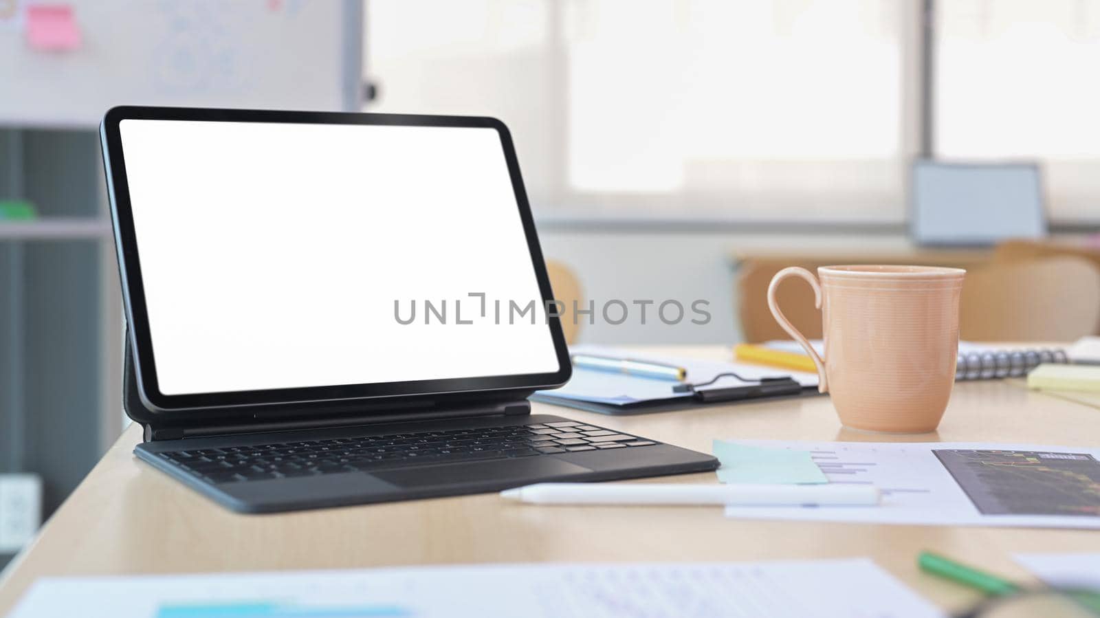Digital tablet with wireless keyboard, coffee cup and financial documents on office desk.