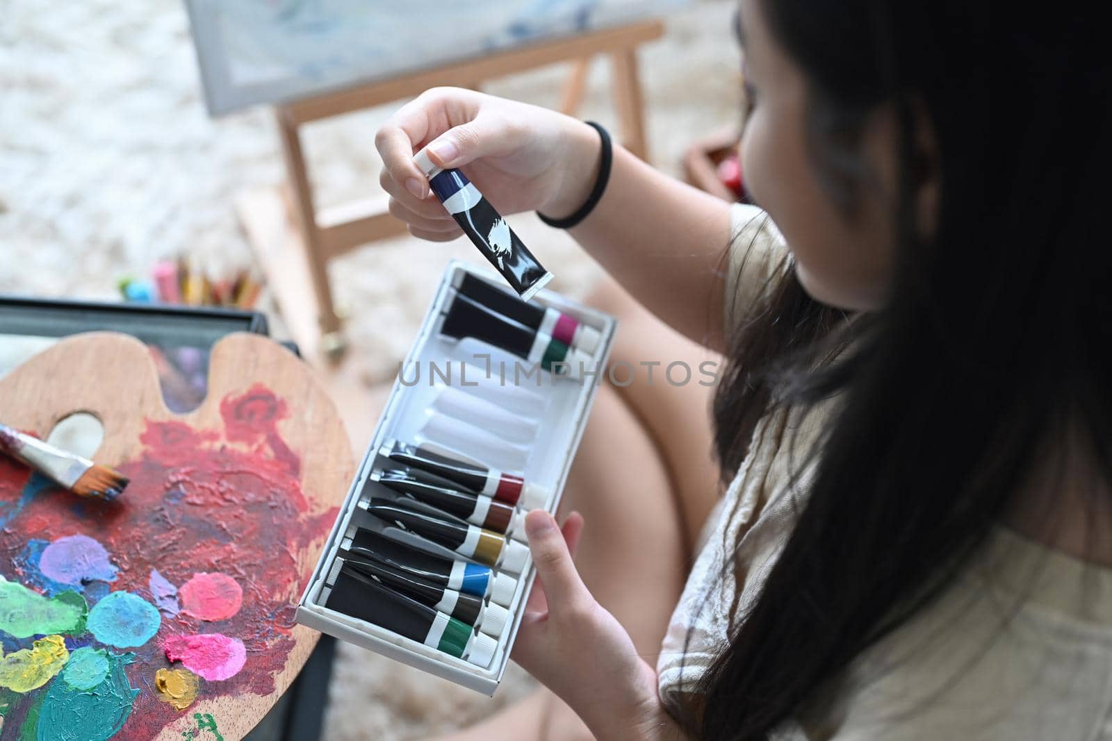 Cropped shot of little girl hand choosing acrylic paint tube for her artwork.