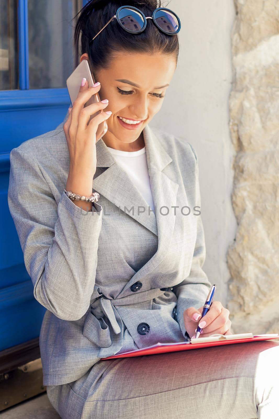 Portrait of happy attractive young businesswoman talking on smart phone near door outdoors.