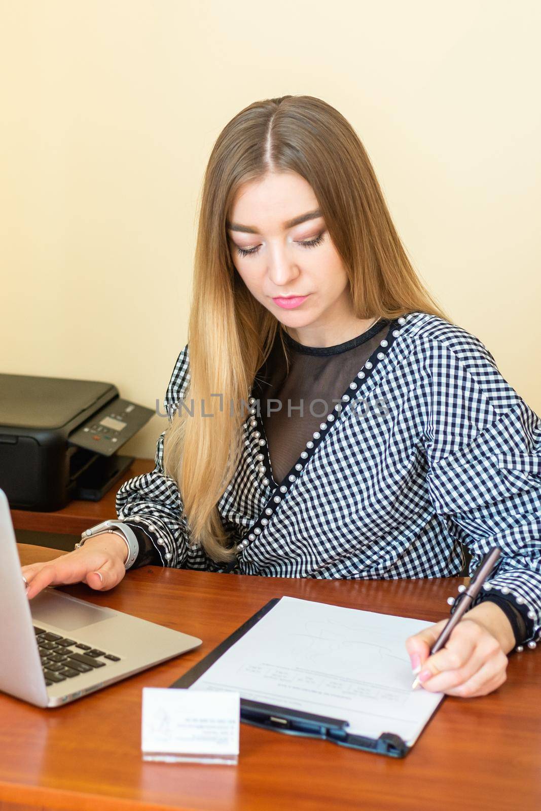 Business woman is writing on a document with laptop at home office.