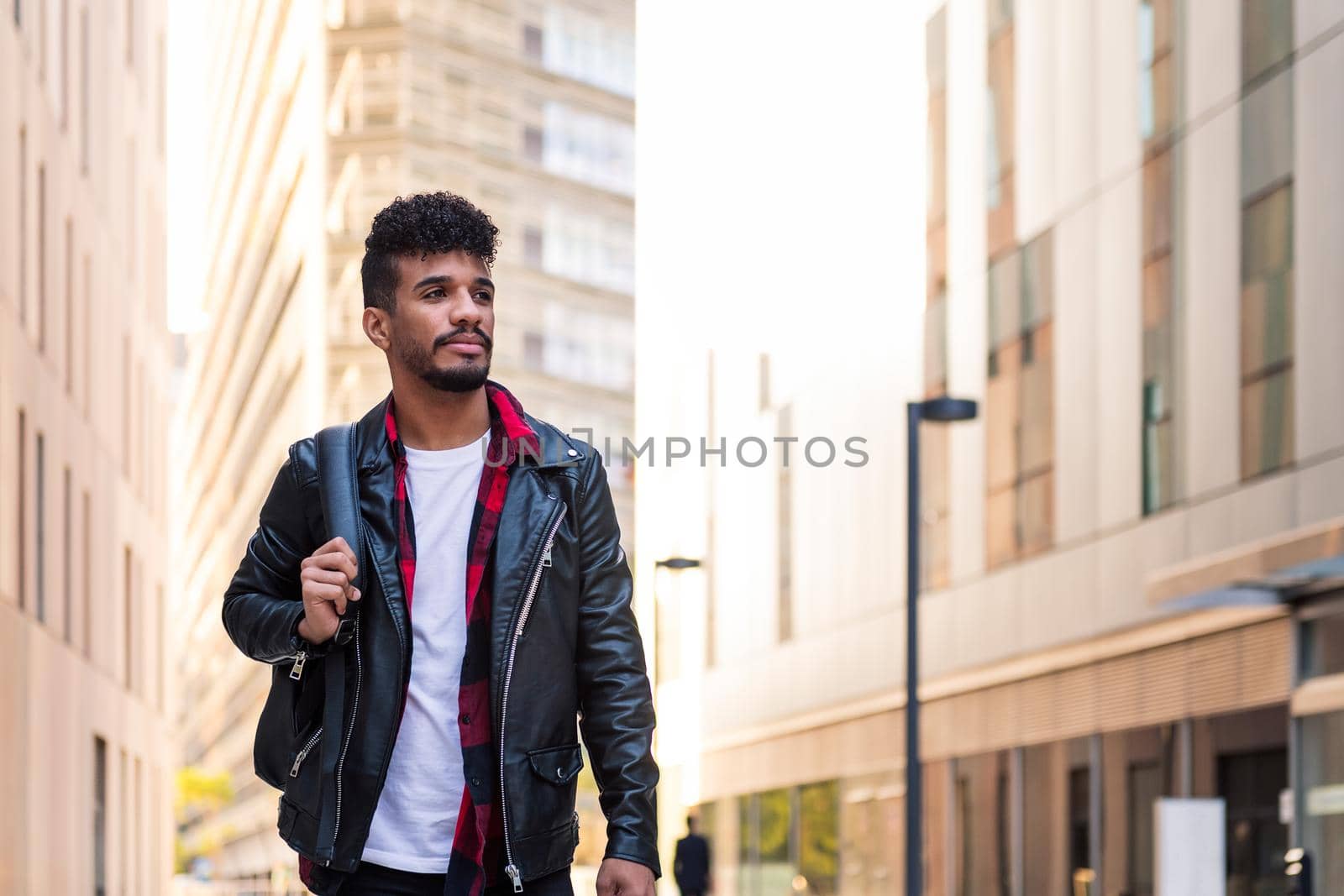 stylish young latin student walking in the city with his backpack, concept of urban lifestyle