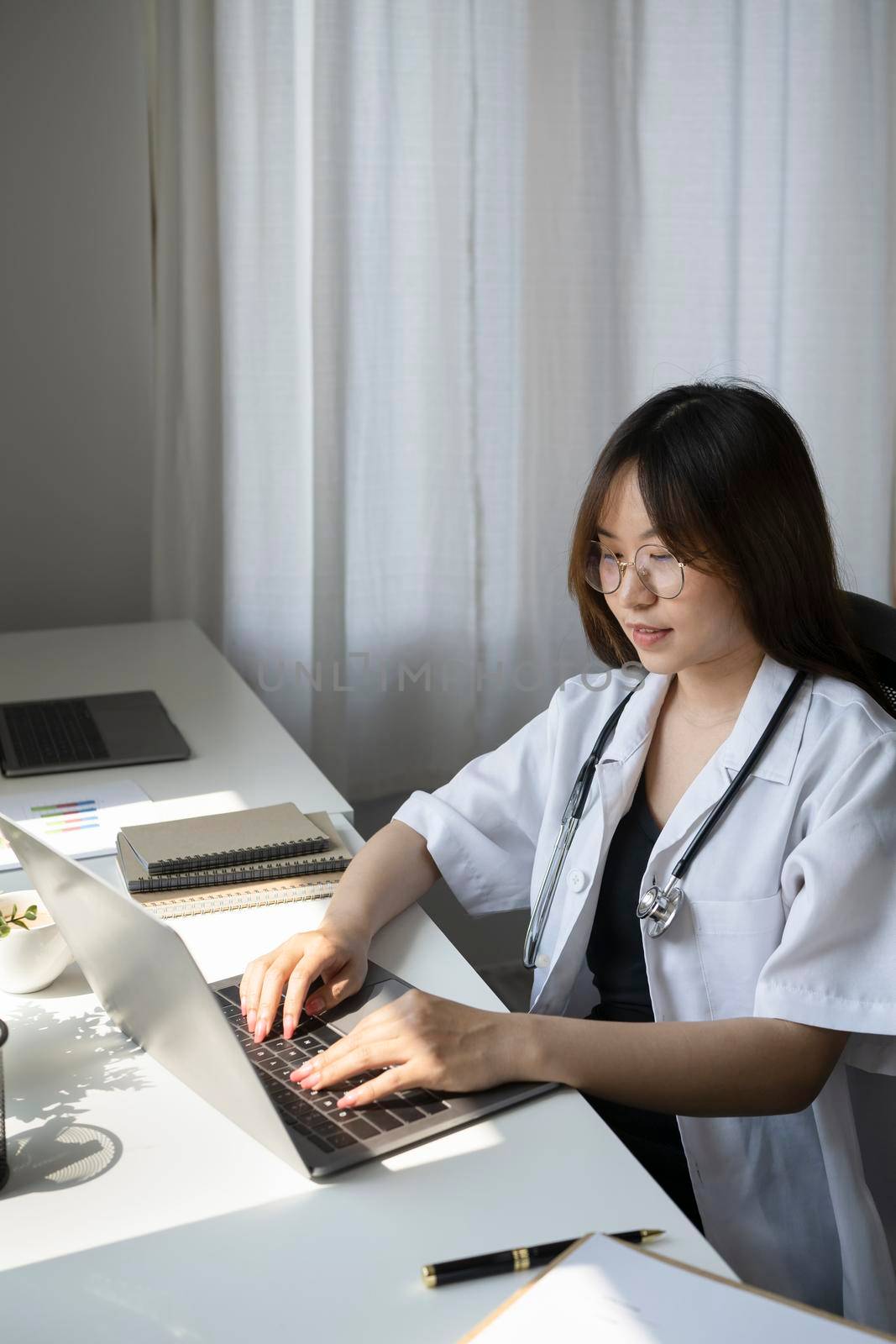 Attractive female doctor is working with documents and laptop in her medical office.