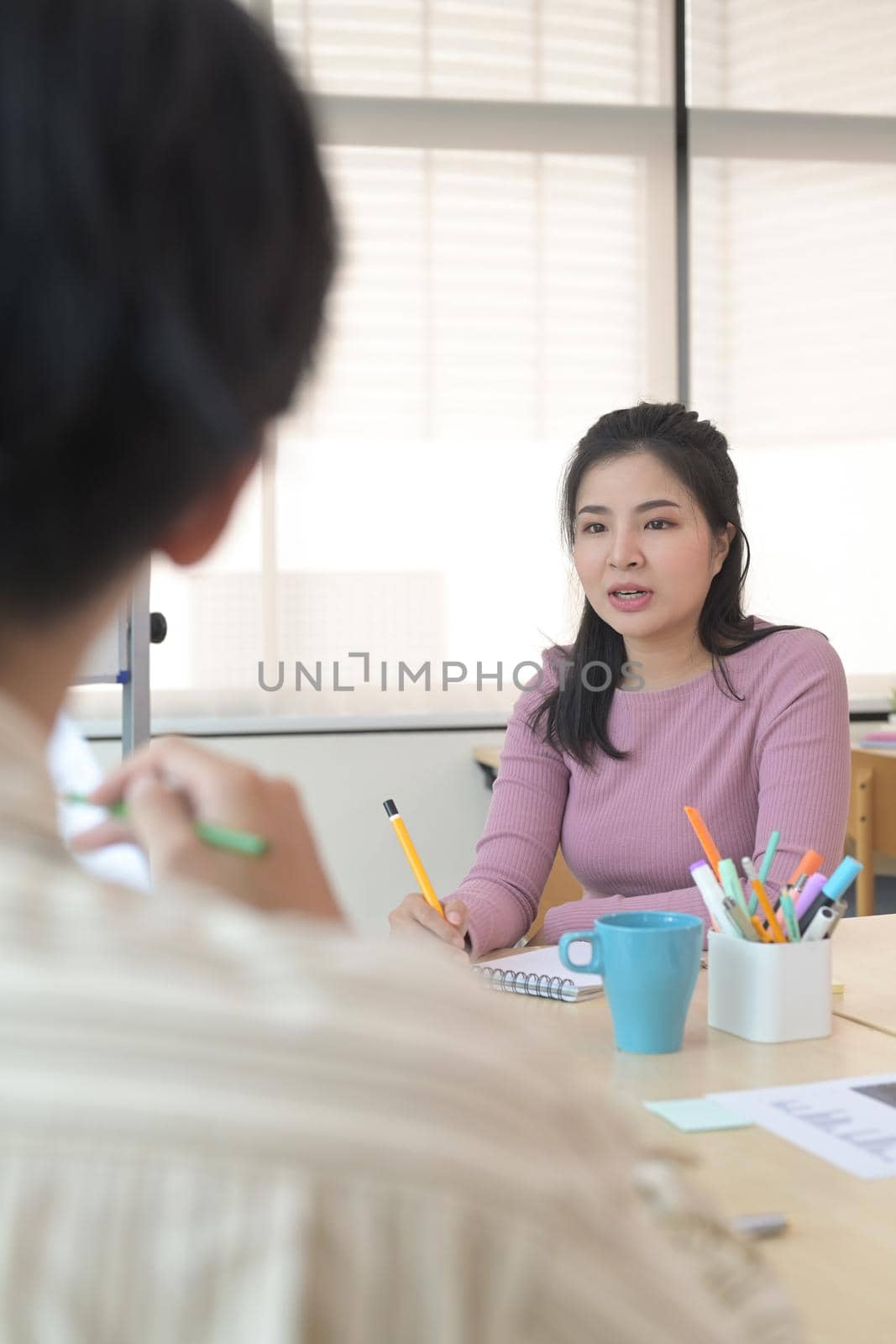 Focused female startup business leader explaining new strategies to coworkers during meeting in office.