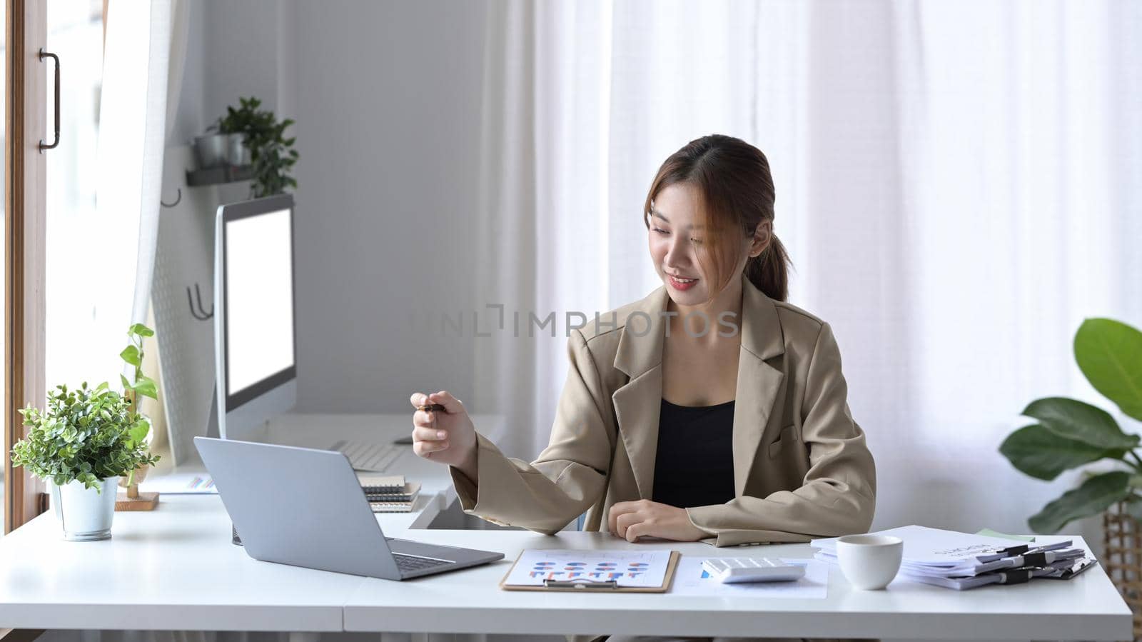 Charming young business woman sitting at modern workplace and using laptop computer.