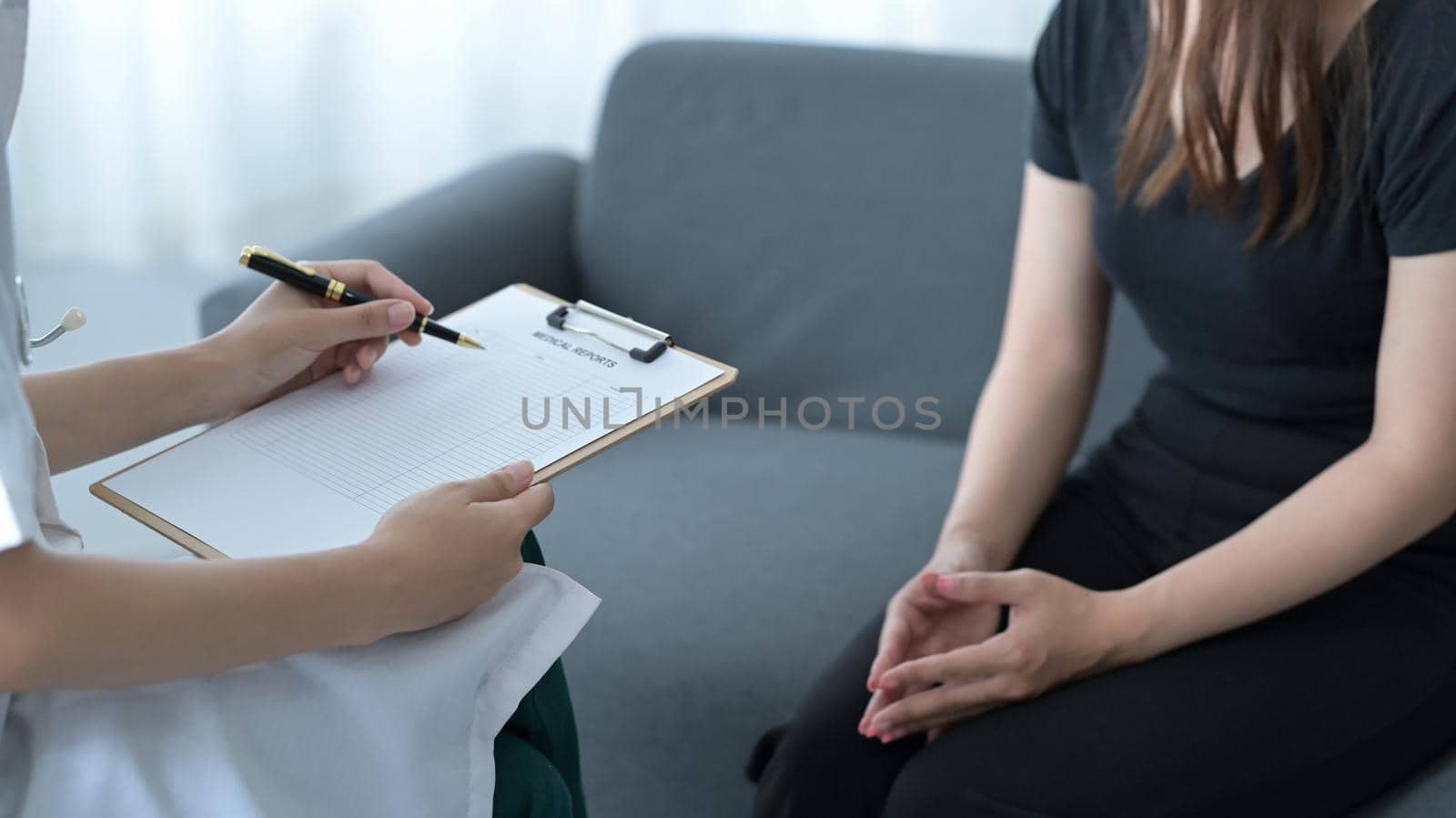 Professional physician wearing white coat talking with patient and signing medical paper at appointment visit in clinic. by prathanchorruangsak