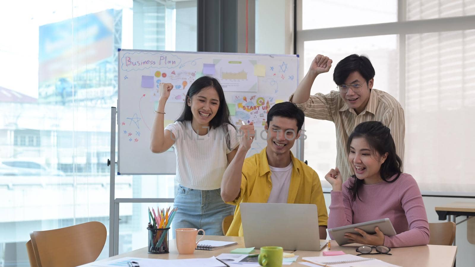 Successful young business team celebrating corporate victory together in office.