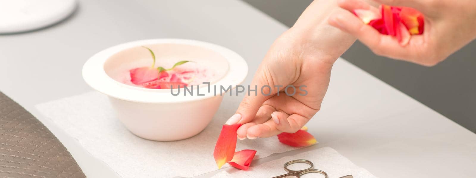 Hands of manicurist decorates bowl of water and table with petals in spa.