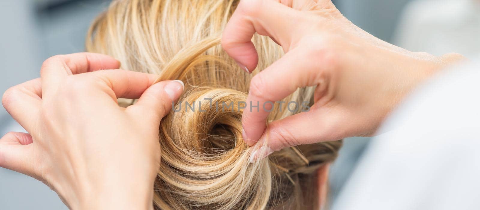 Close up rear view of hairdresser making hairstyle for long hair of blonde woman.