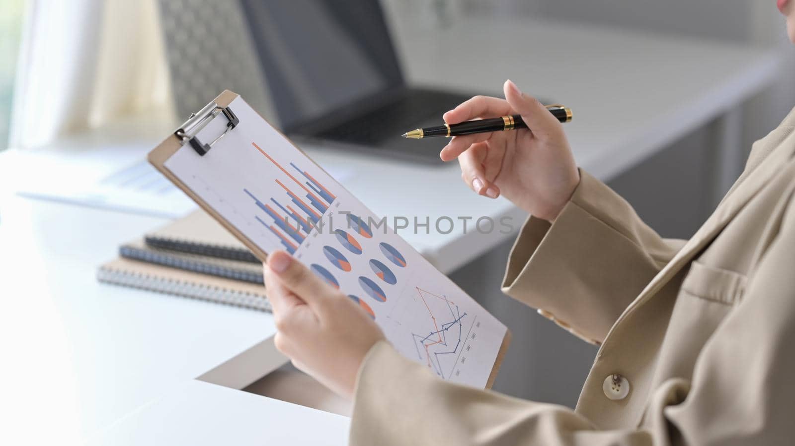 Cropped shot businesswoman sitting at comfortable workplace and analyzing financial graph.