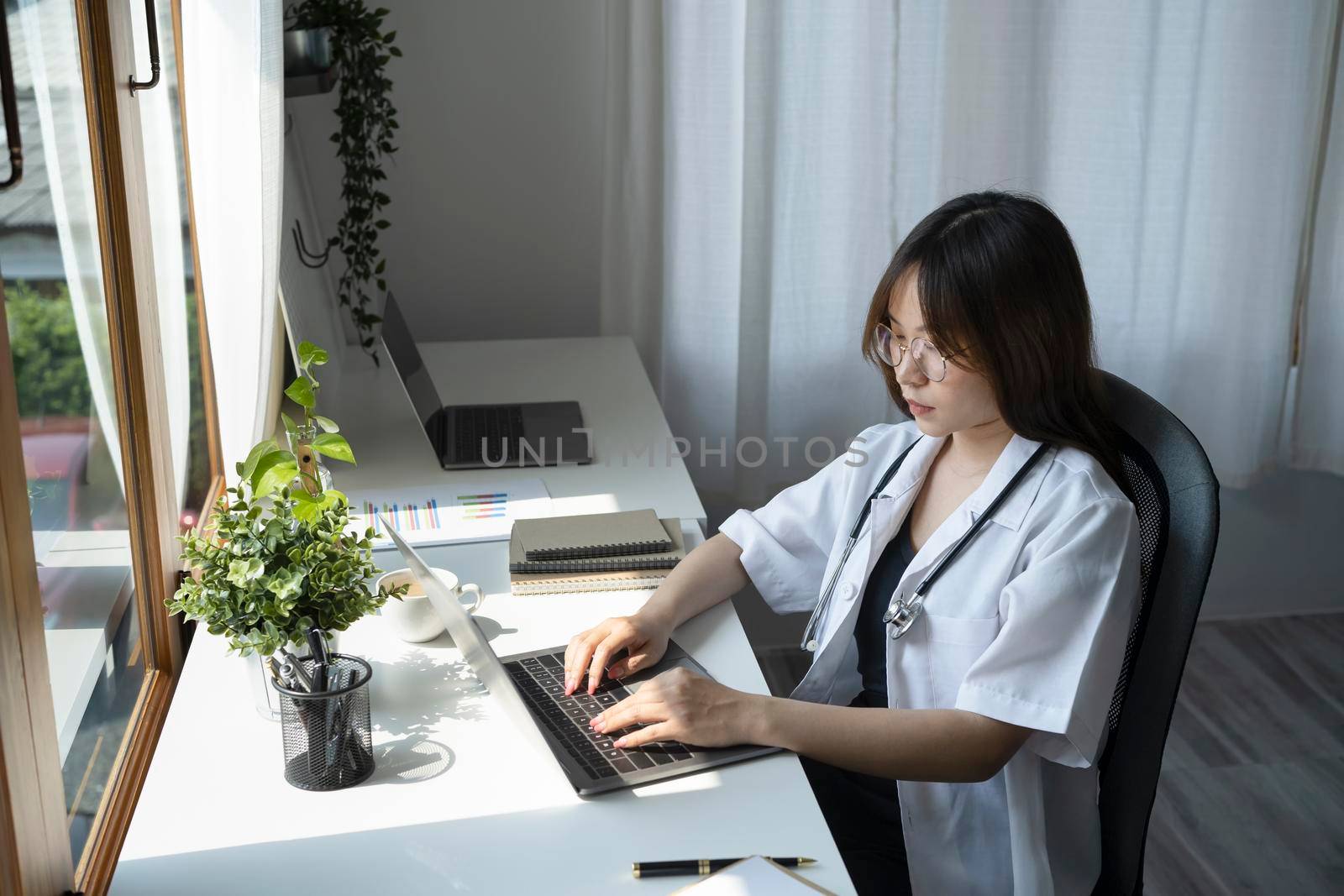 Focused female doctor in white uniform working in medical office.