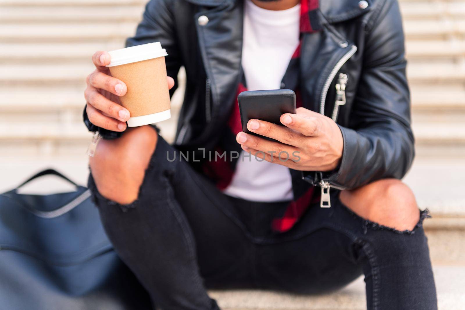 detail of the hands of an unrecognizable stylish young man consulting the phone with a coffee in his hand, concept of technology and urban lifestyle