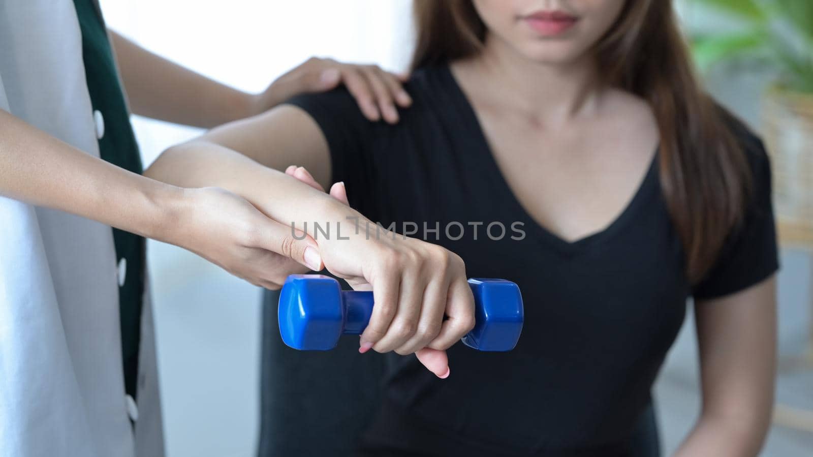 Physiotherapist giving exercise with dumbbell treatment about arm and shoulder of female patient. Physical therapy concept