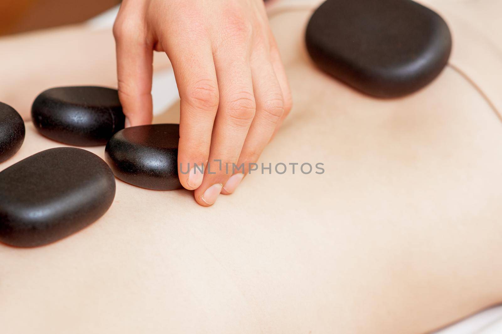 Back massage on back of woman with black hot stones close up.