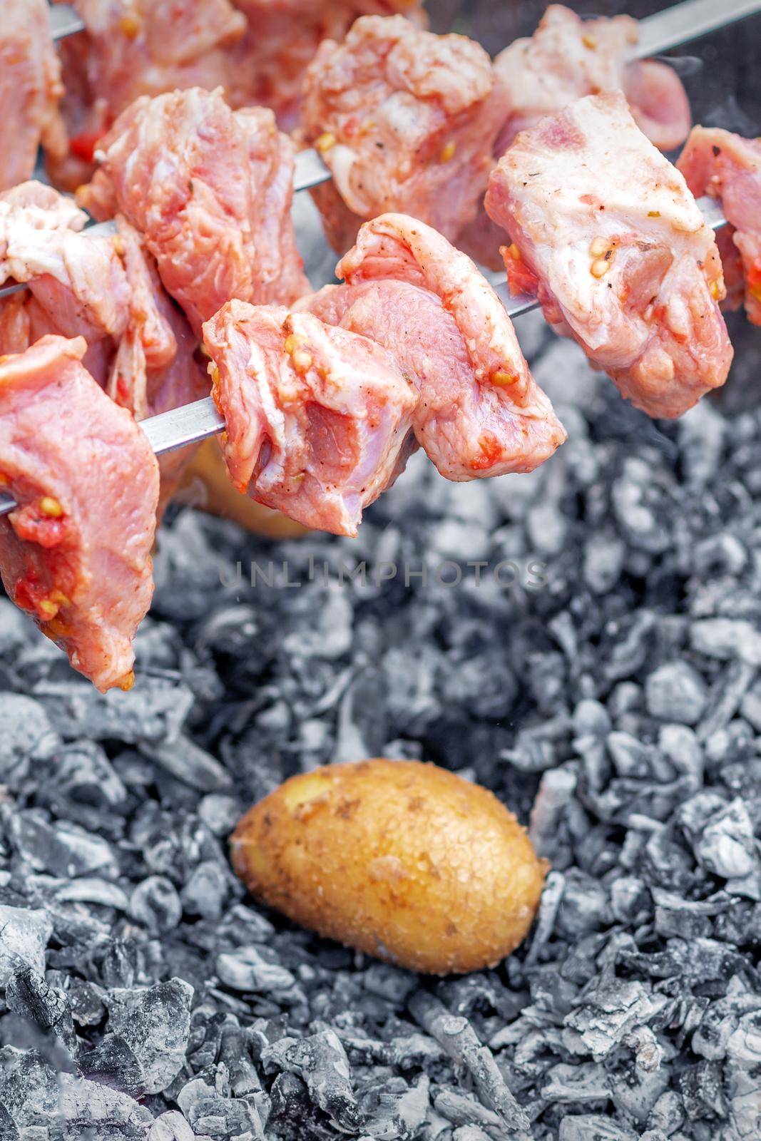 Hands of man prepares barbecue meat with potatoes on skewer by grill on fire outdoors. Concept of lifestyle rustic food preparation