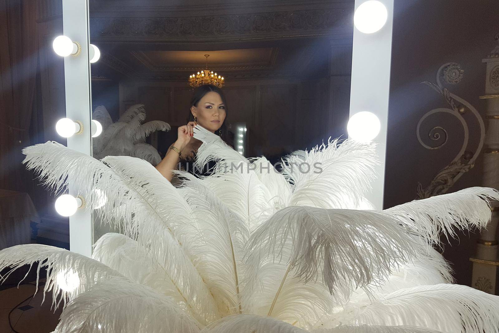 Beautiful asian young woman and decorative ostrich feathers on a gold table next to a make-up mirror. by Rom4ek