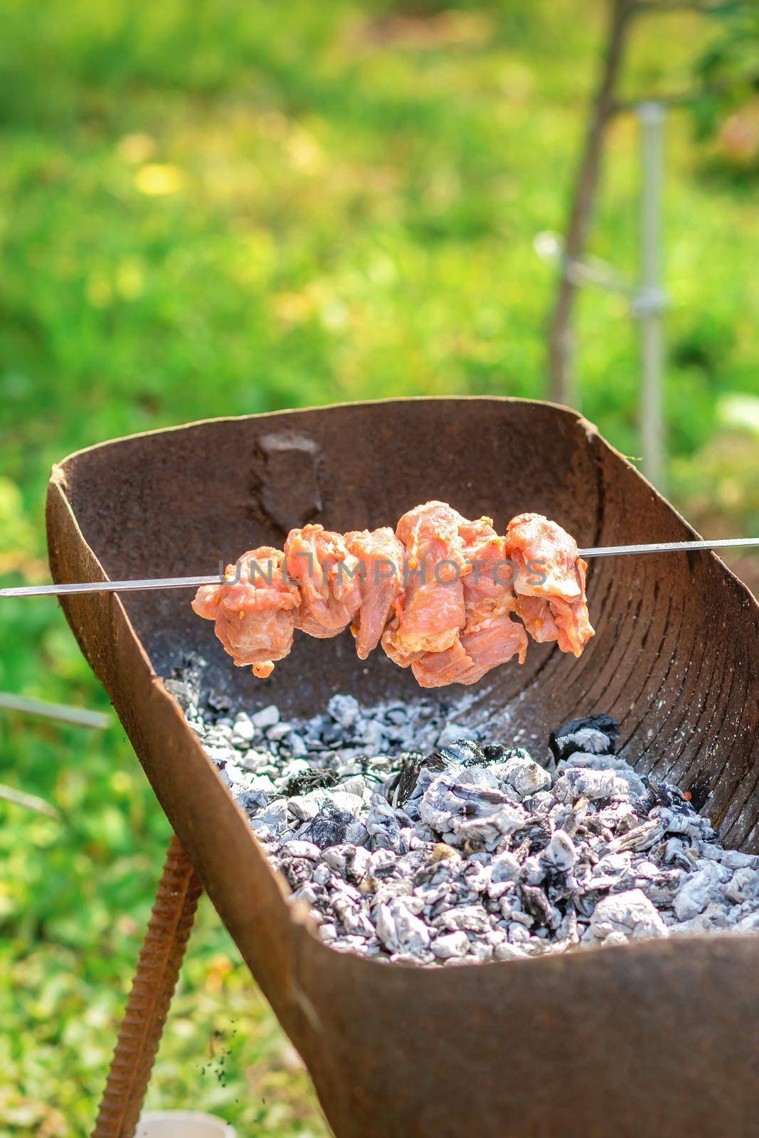 Hands of man prepares barbecue meat on skewer by grill on fire outdoors