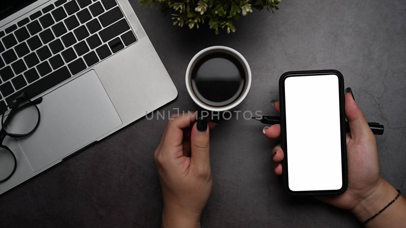 Above view woman hand holding mobile phone with empty screen on dark background.