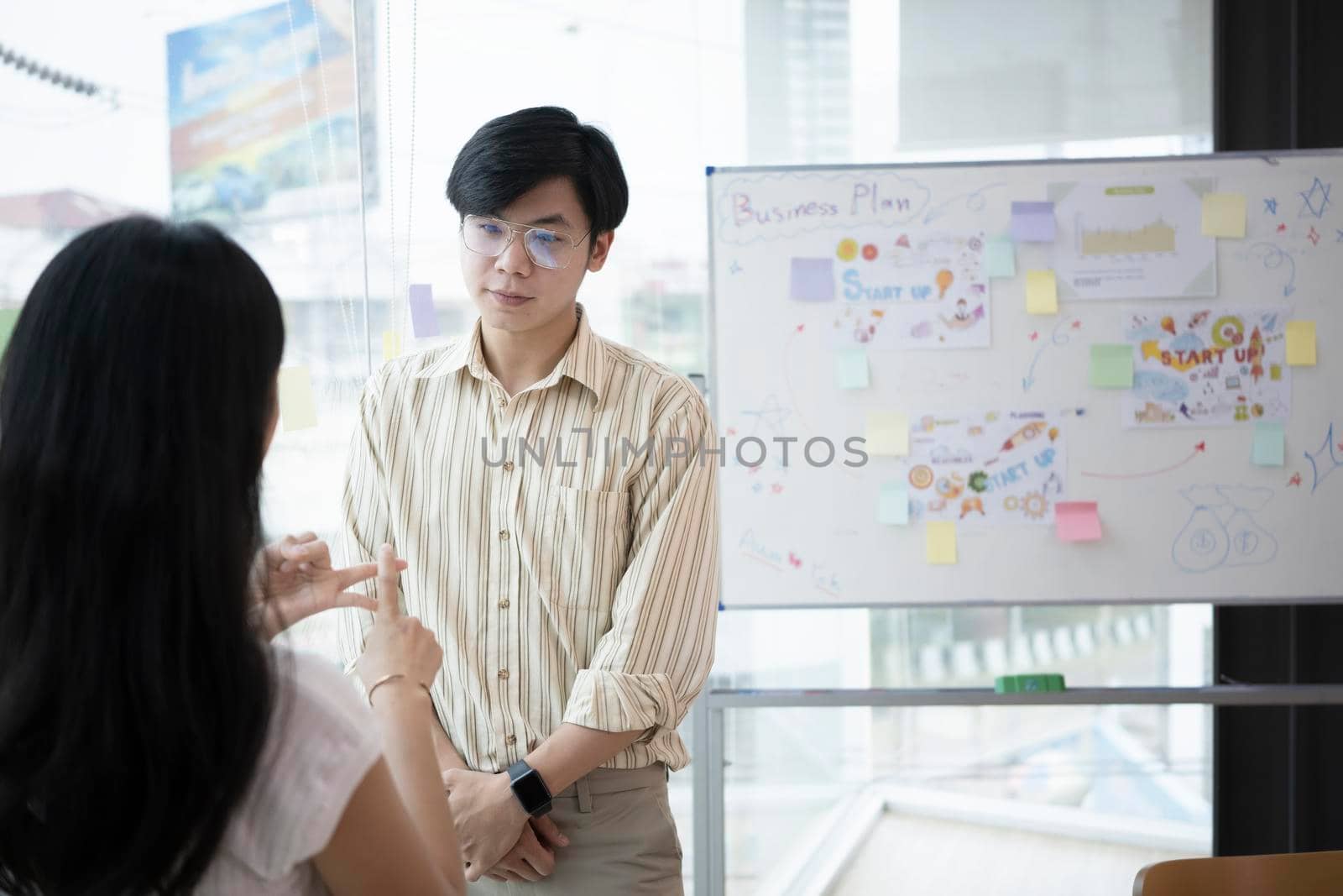 Focused male employee standing near flip board and discussing new marketing strategy with his colleague. by prathanchorruangsak