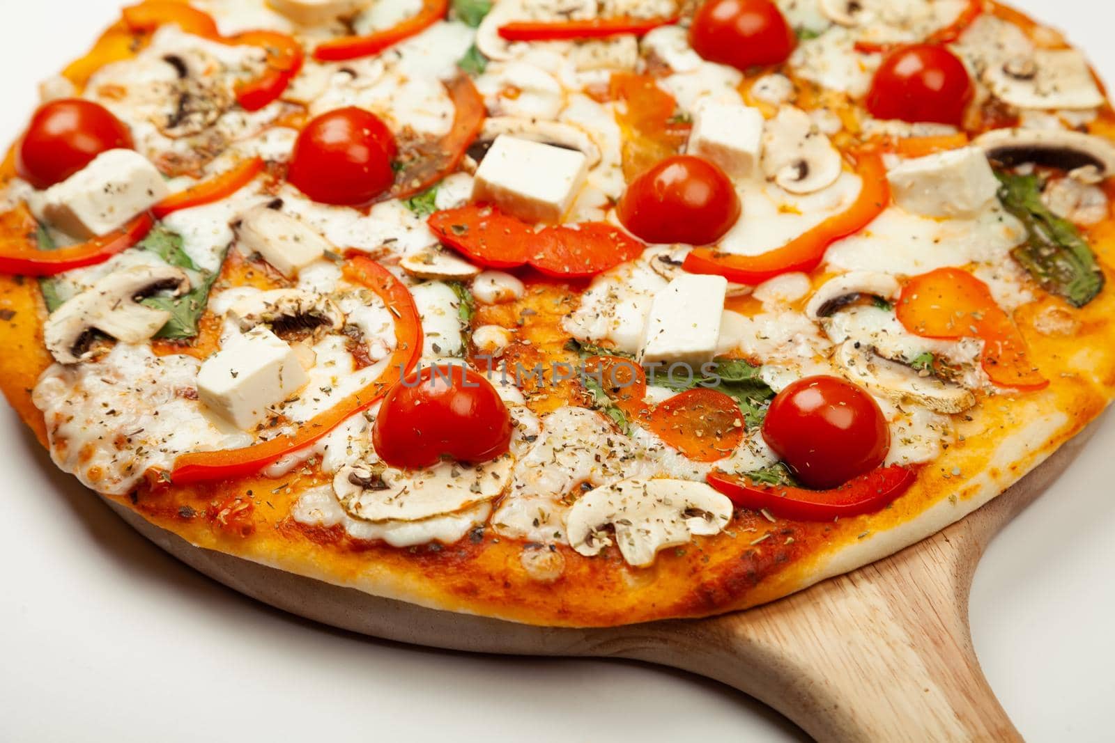 Delicious Vegetarian pizza served on a wooden plate, the ingredients are signature sauce, basil, mozzarella cheese, champignons, bell peppers, cherry tomatoes, feta cheese. Pizzeria promotion poster.
