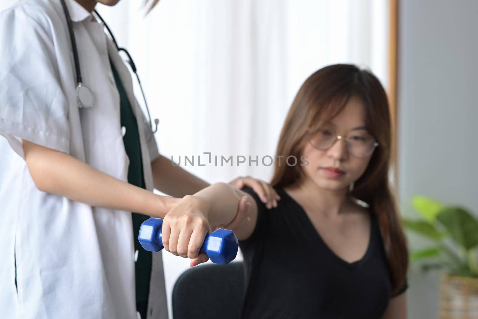 Physiotherapist examining, treating injured arm of female patient in clinic. Rehabilitation physiotherapy concept.