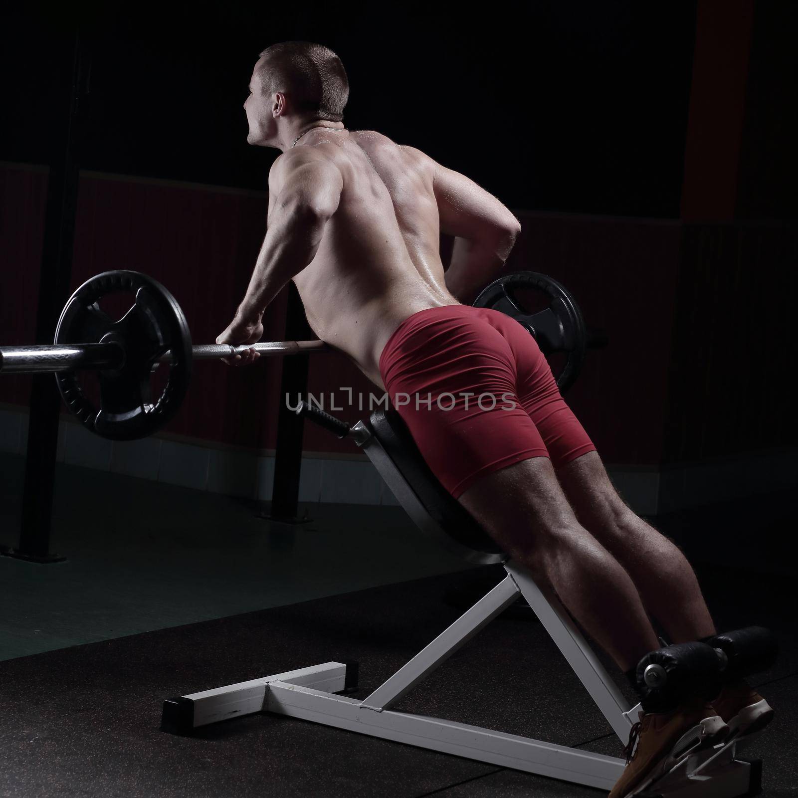 rear view .a man bodybuilder performs an exercise on the simulator by SmartPhotoLab
