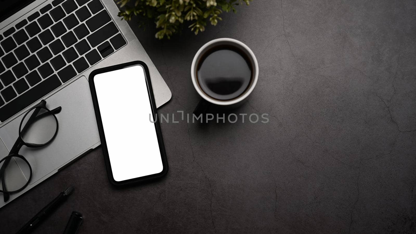 Contemporary workplace with mobile phone, laptop computer and coffee cup on dark stone background.
