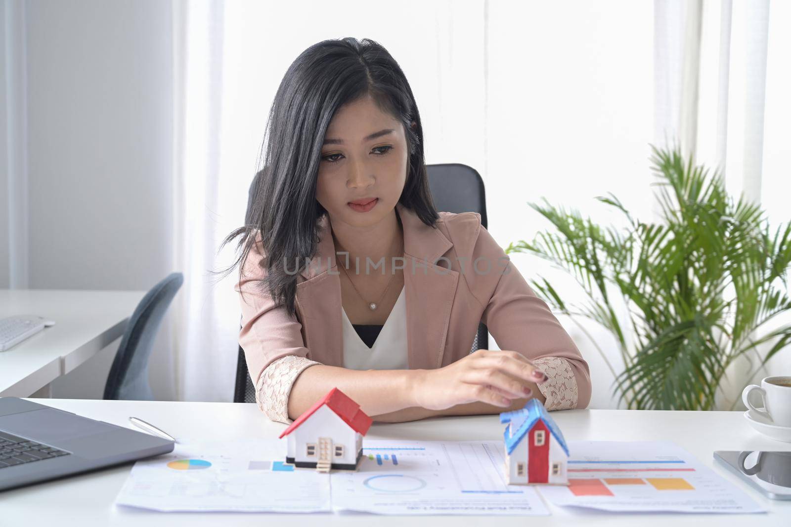 Millennial businesswoman sitting in office with house model. Accounting, property investment concept.