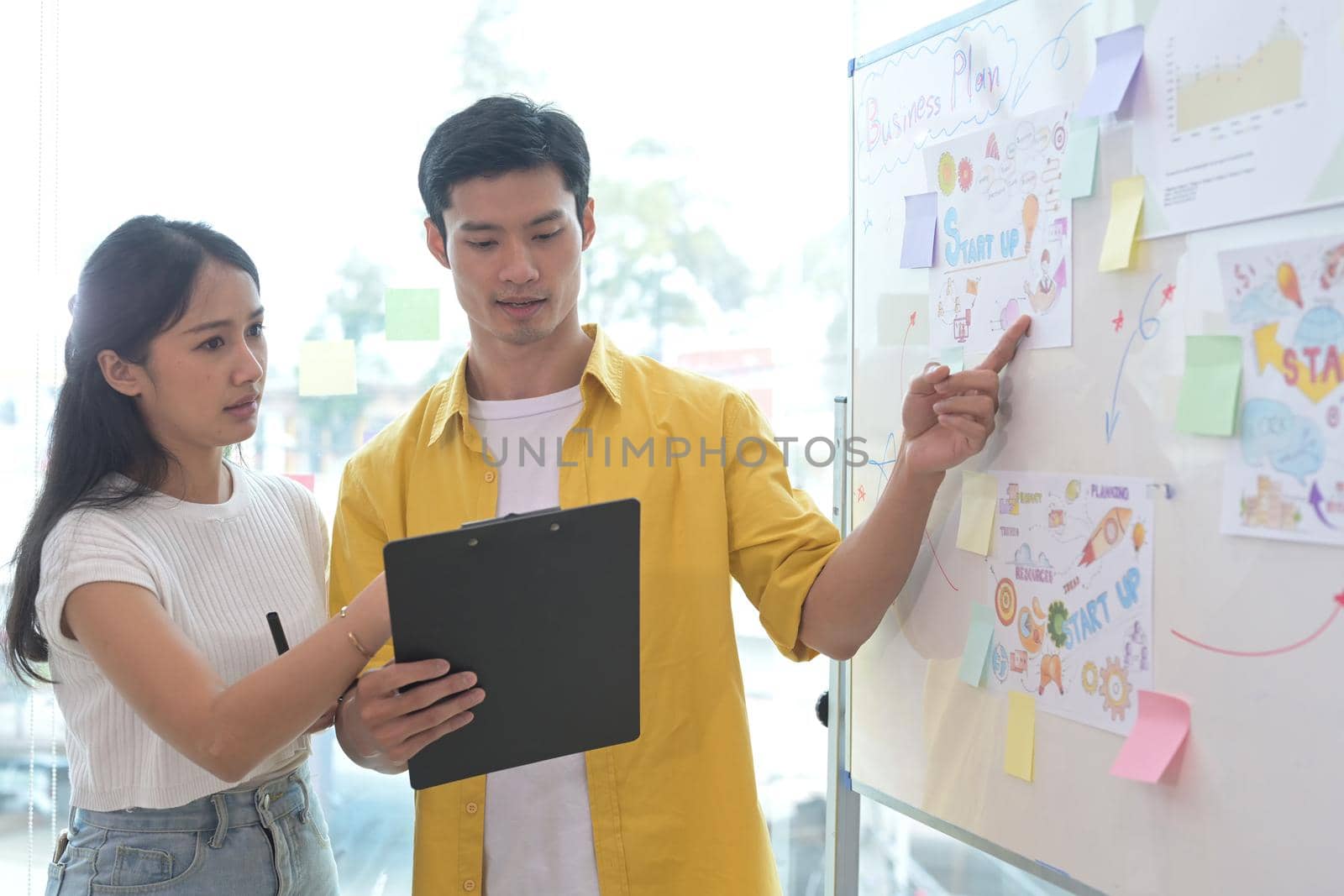 Young asian woman and her colleague giving presenting new marketing strategy on flip chart. by prathanchorruangsak