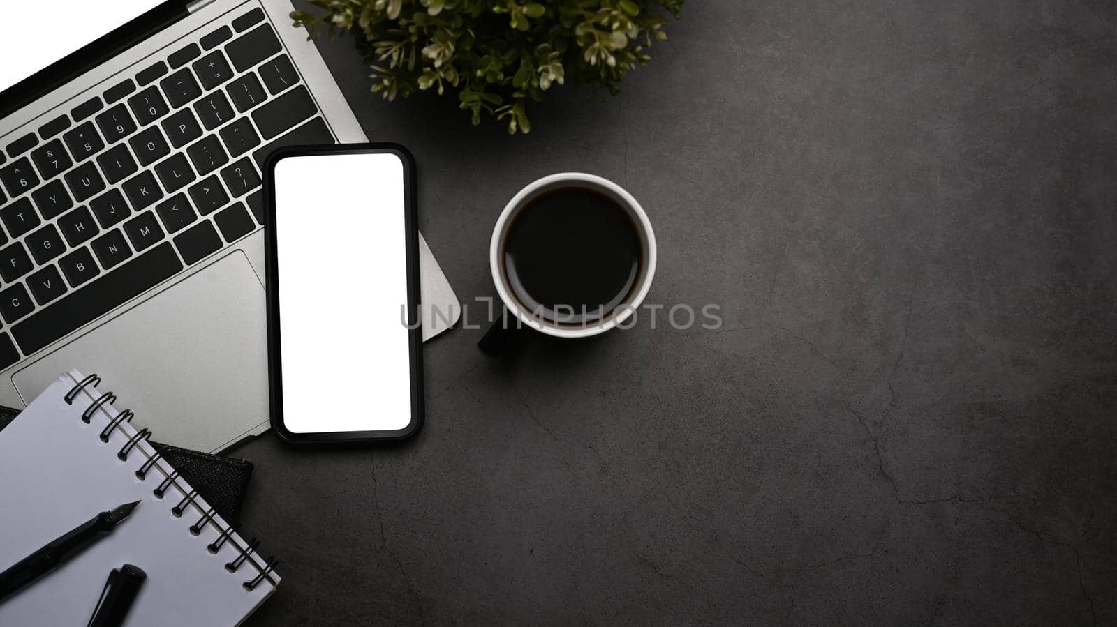 Mobile phone, laptop computer and coffee cup on dark stone background. Flat lay, Top view.