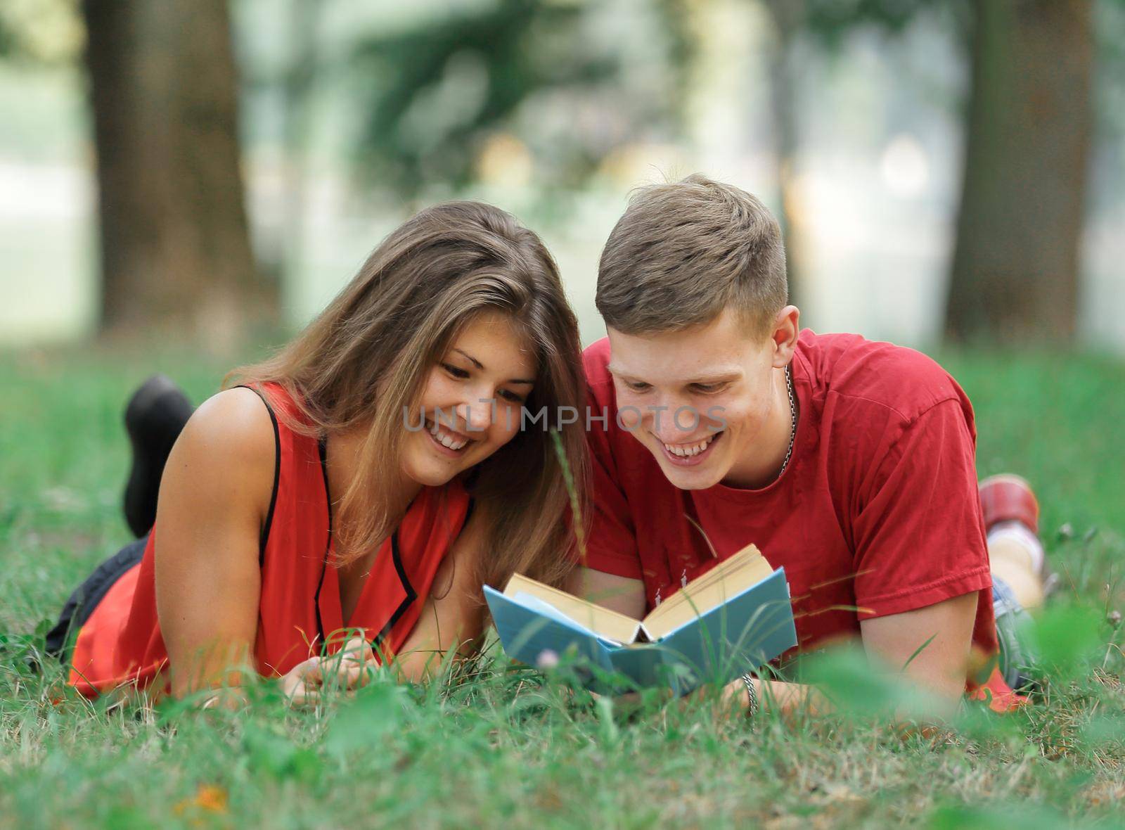couple of students lying on the grass in the Park and reading a book.