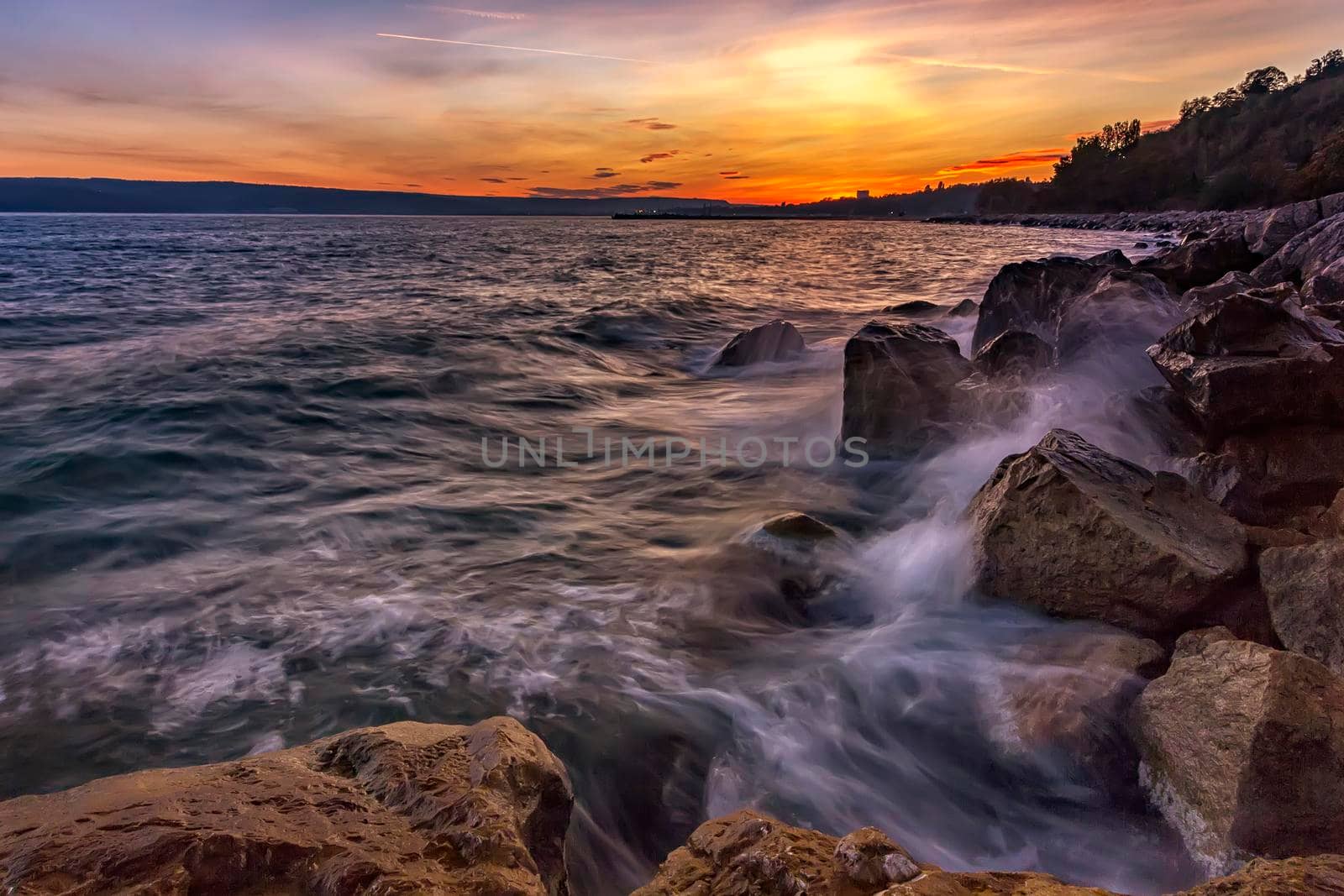 Sunset over the sea with splash waves on the rocks