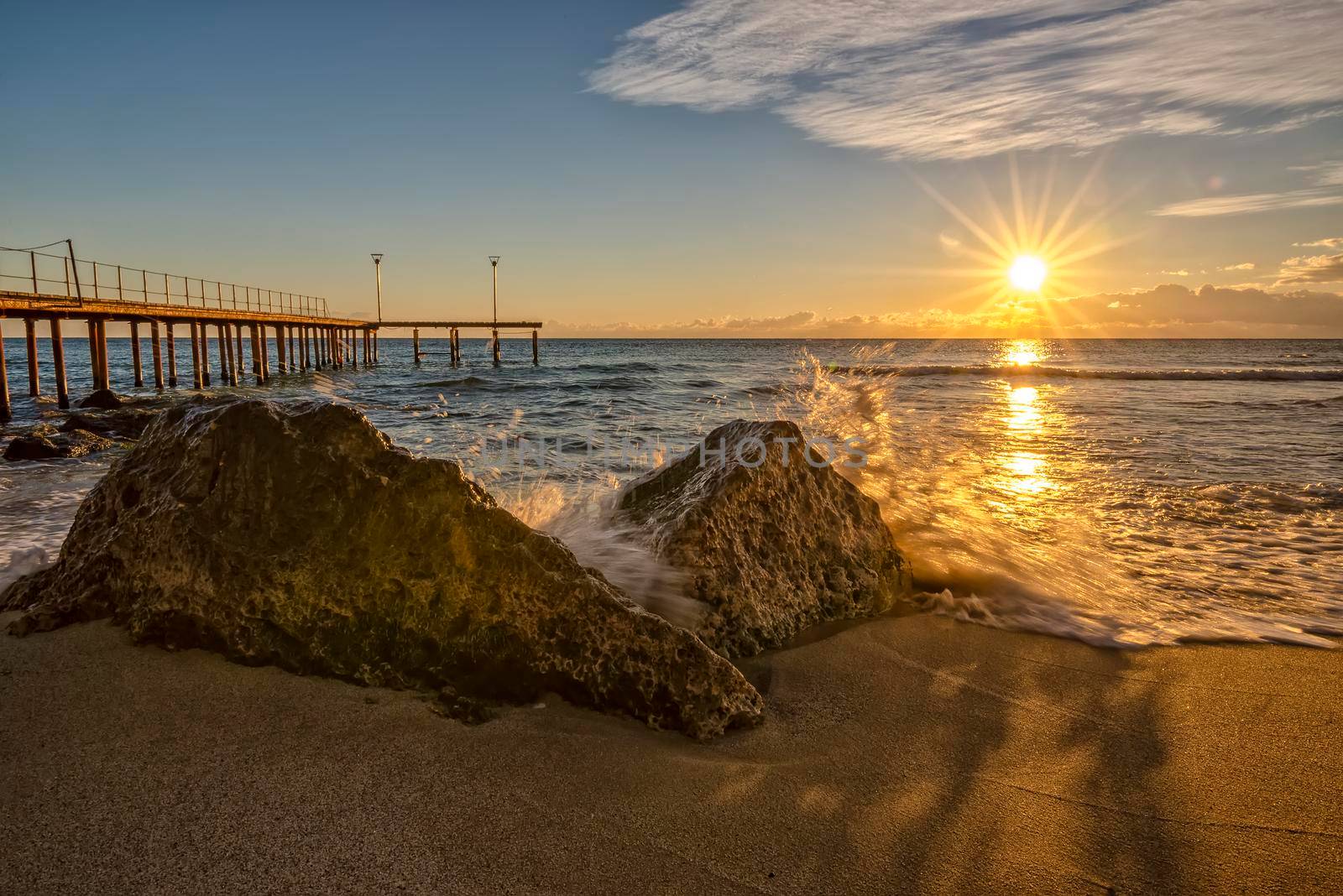 Sunrise over the sea with wave splashing on the rocks.