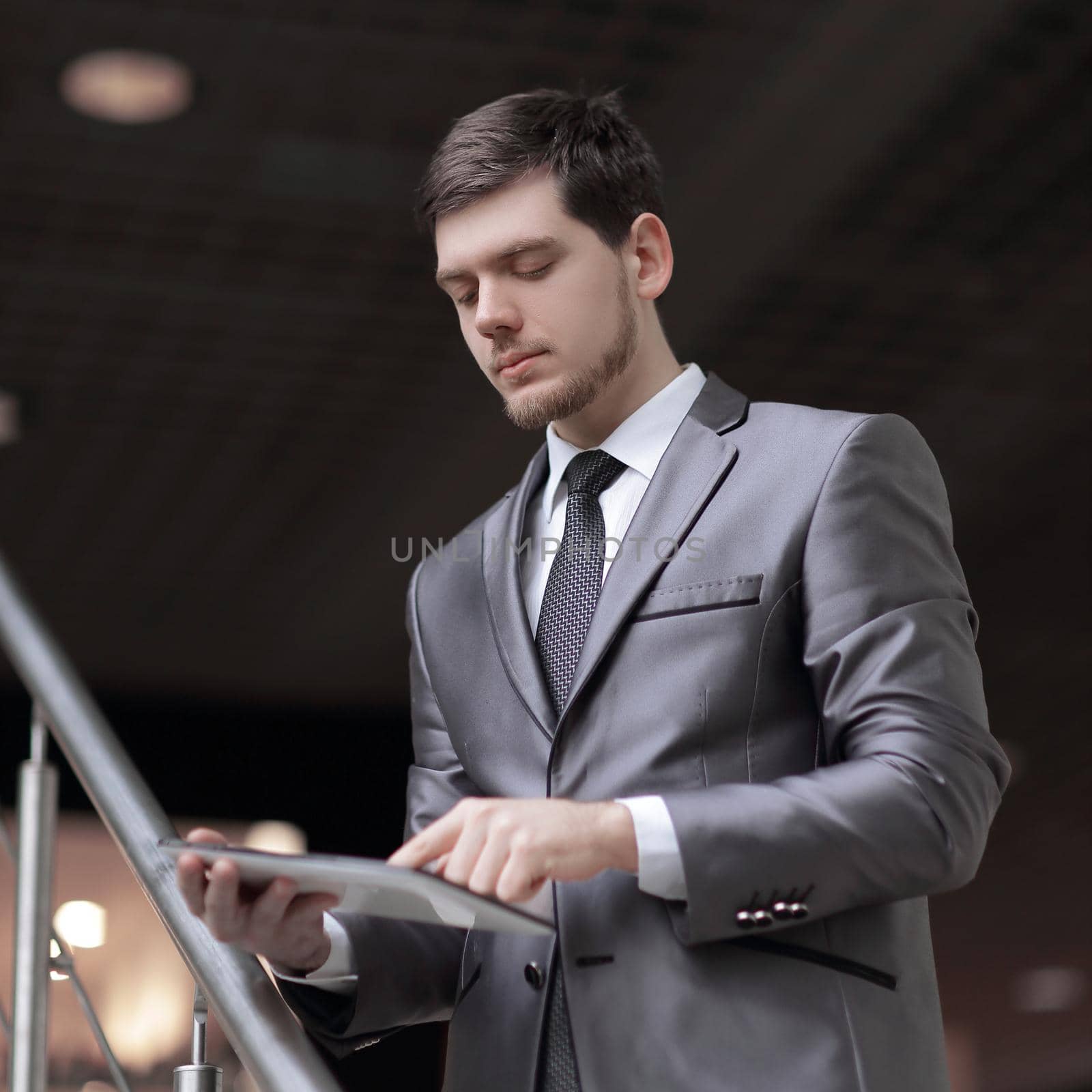 Handsome businessman standing on steps using tablet in office building.