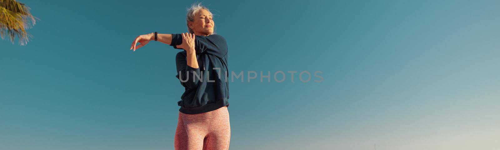 Motivated female in sportswear doing arm workout on the sports ground on a sunny day by the waterfront