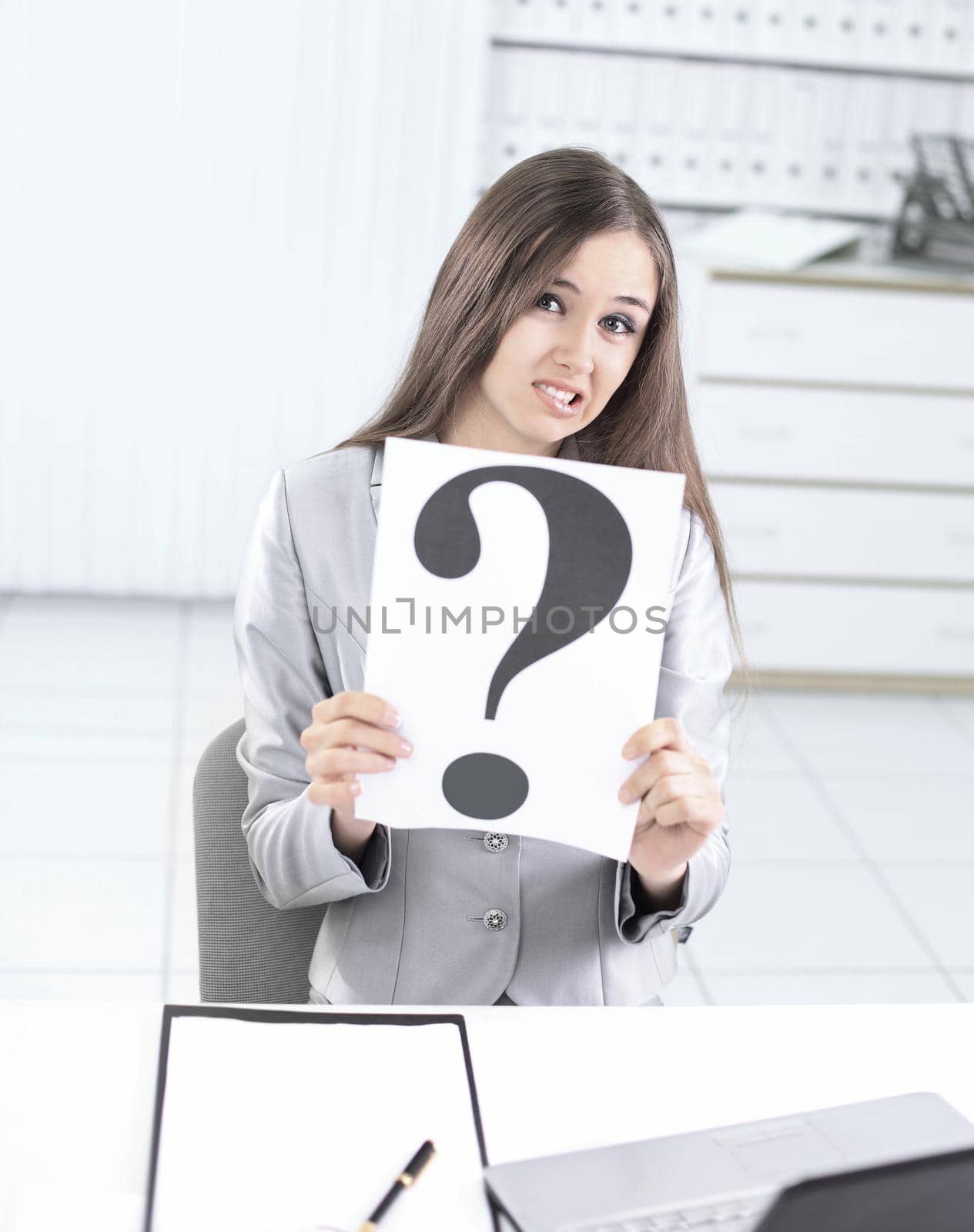 upset business woman holding a question mark ,sitting behind a Desk .photo with copy space.