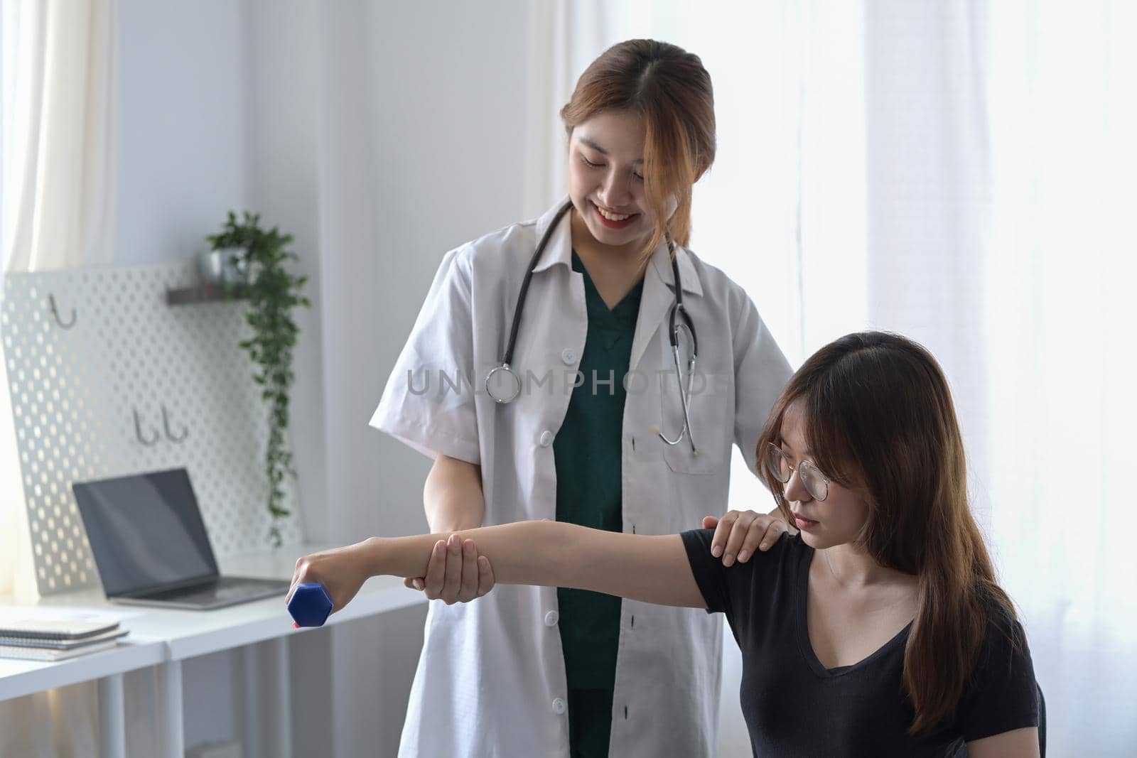 Female physiotherapist helping young patient with lifting dumbbell exercises in clinic. by prathanchorruangsak