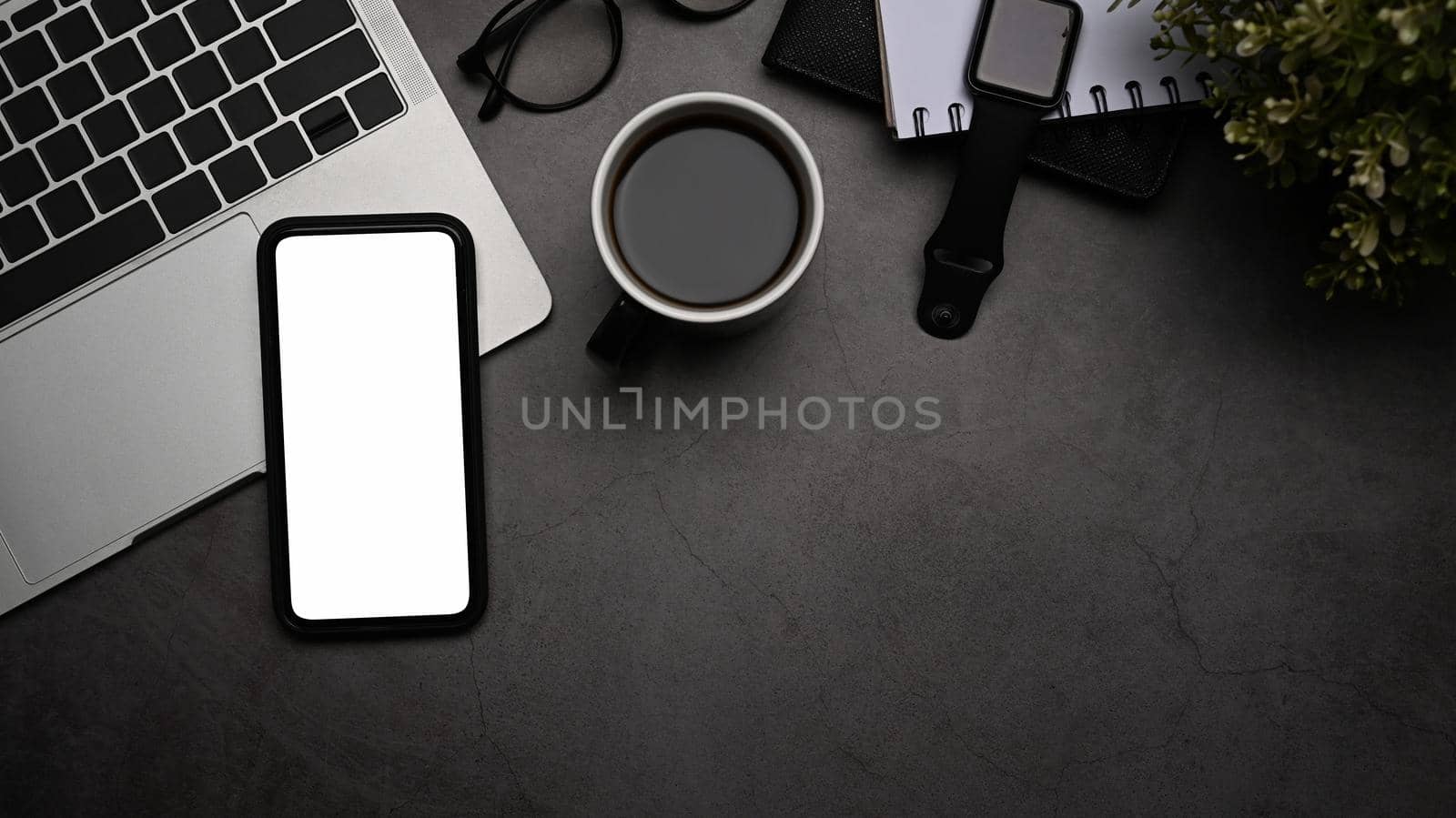 Smart phone with white screen, laptop computer, smart watch, coffee cup and eyeglasses on black table. Flat lay.