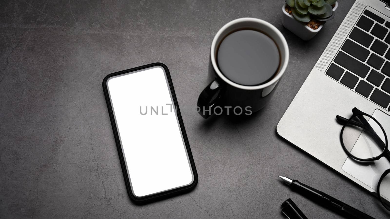 Top view modern workplace with mobile phone, laptop computer and coffee cup on dark stone background.
