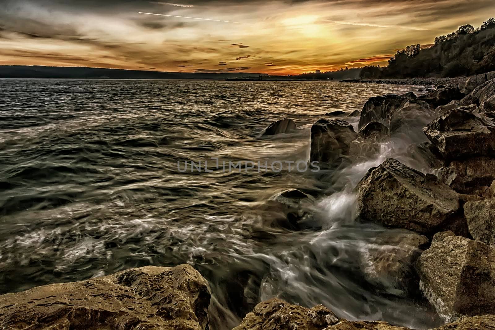 Sunset over the sea with splash waves on the rocks
