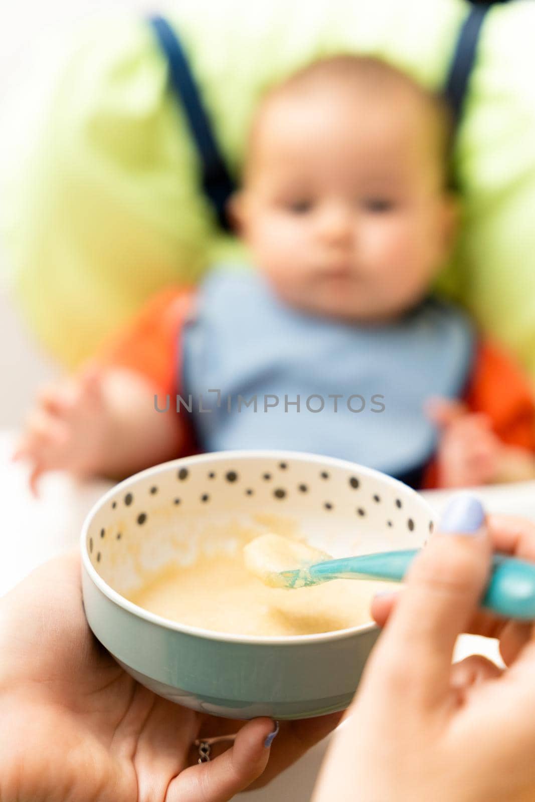 Cheerful baby child eats food with spoon. Portrait of happy kid boy in high chair. High quality photo