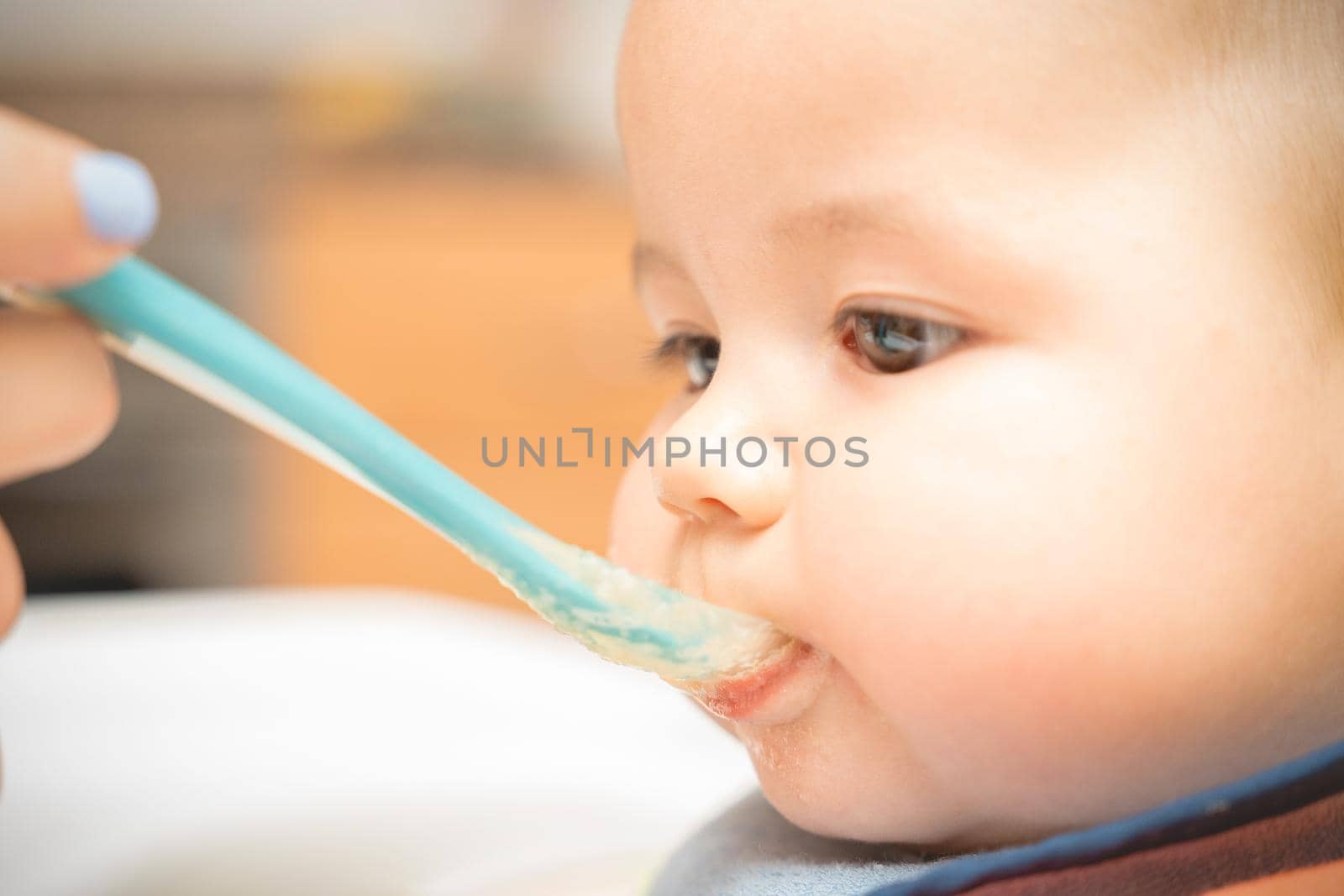 Cheerful baby child eats food with spoon. Portrait of happy kid boy in high chair. High quality photo