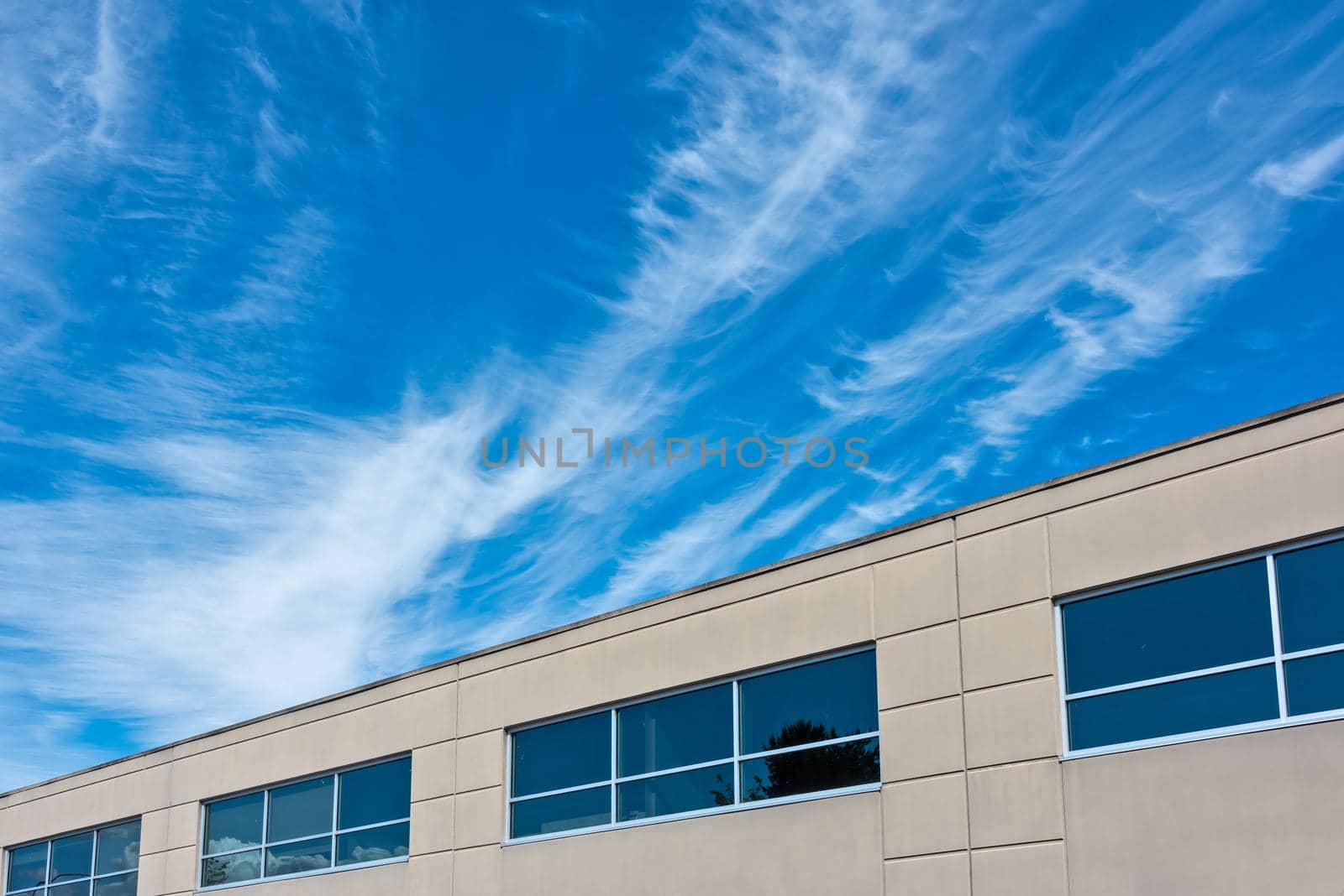 Top of the office building with windows on blue and cloudy sky background.