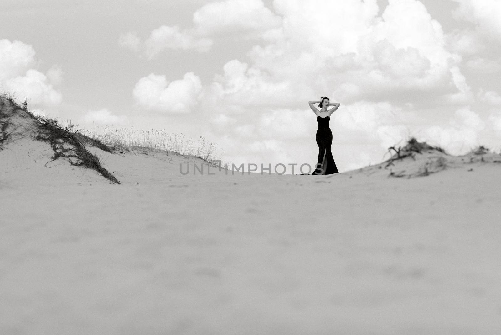 girl in a black long dress in a sandy desert under a blue sky