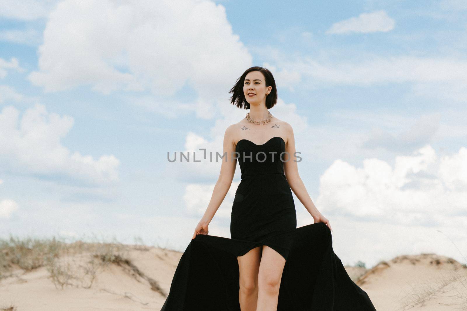 girl in a black long dress in a sandy desert under a blue sky