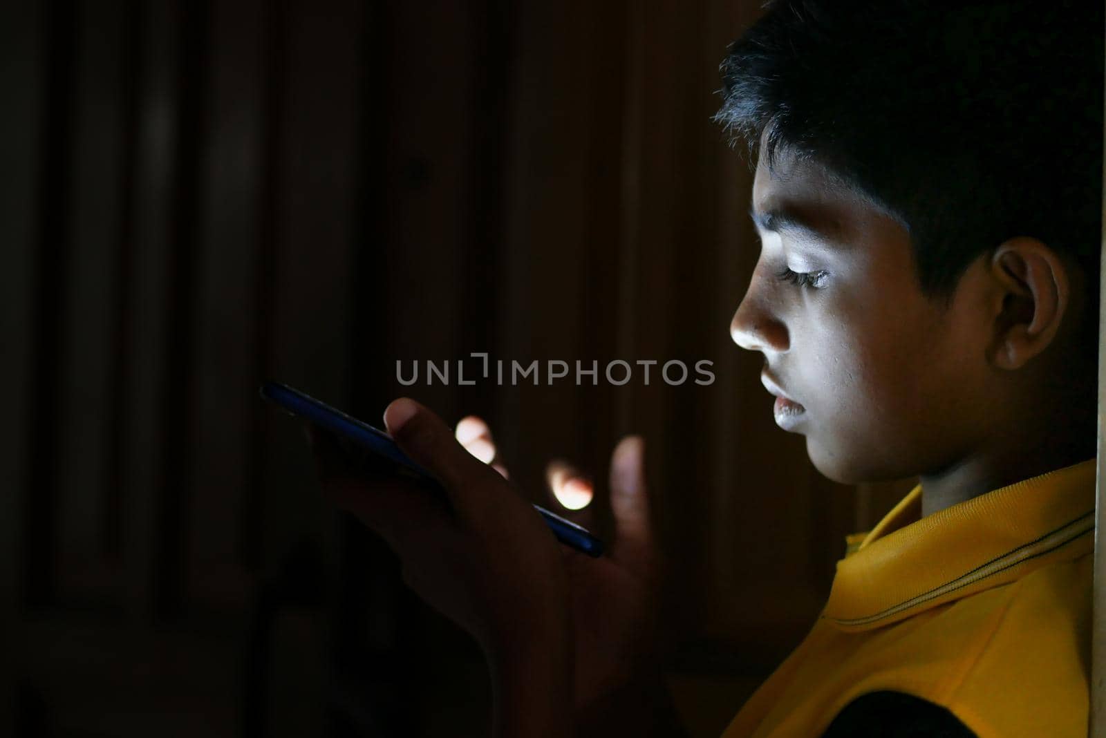 teenage boy sitting on sofa using smart phone at night .