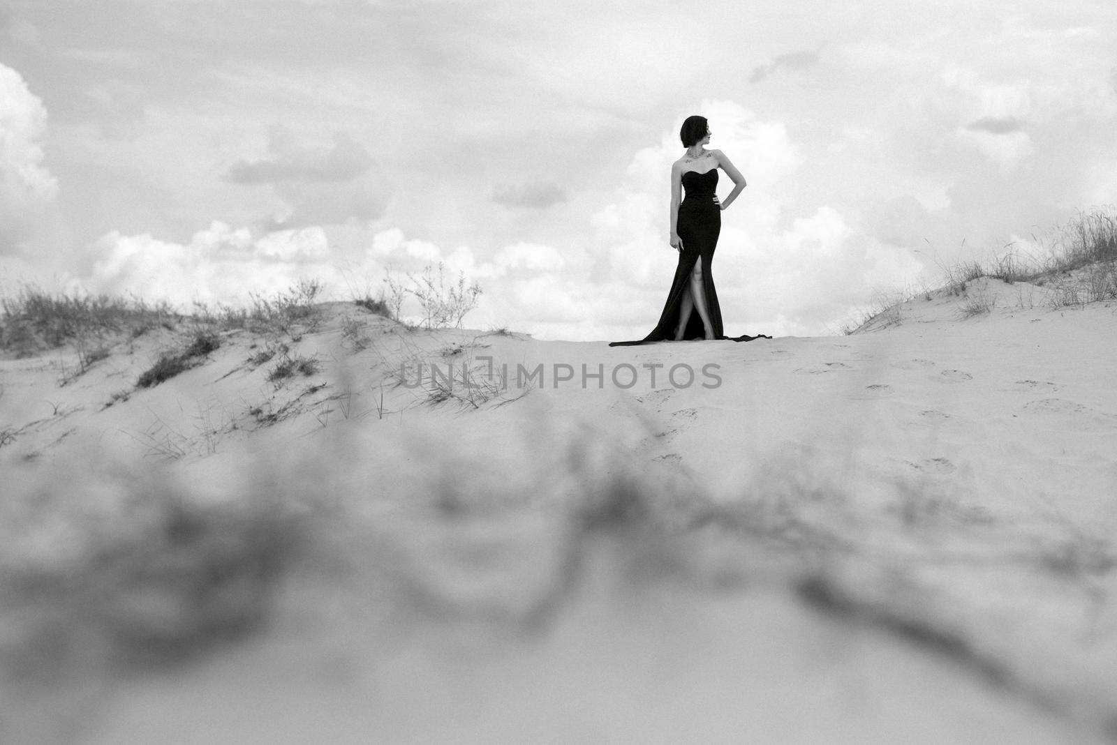 girl in a black long dress in a sandy desert under a blue sky