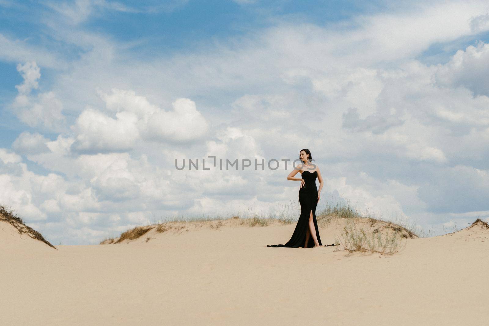 girl in a black long dress in a sandy desert under a blue sky